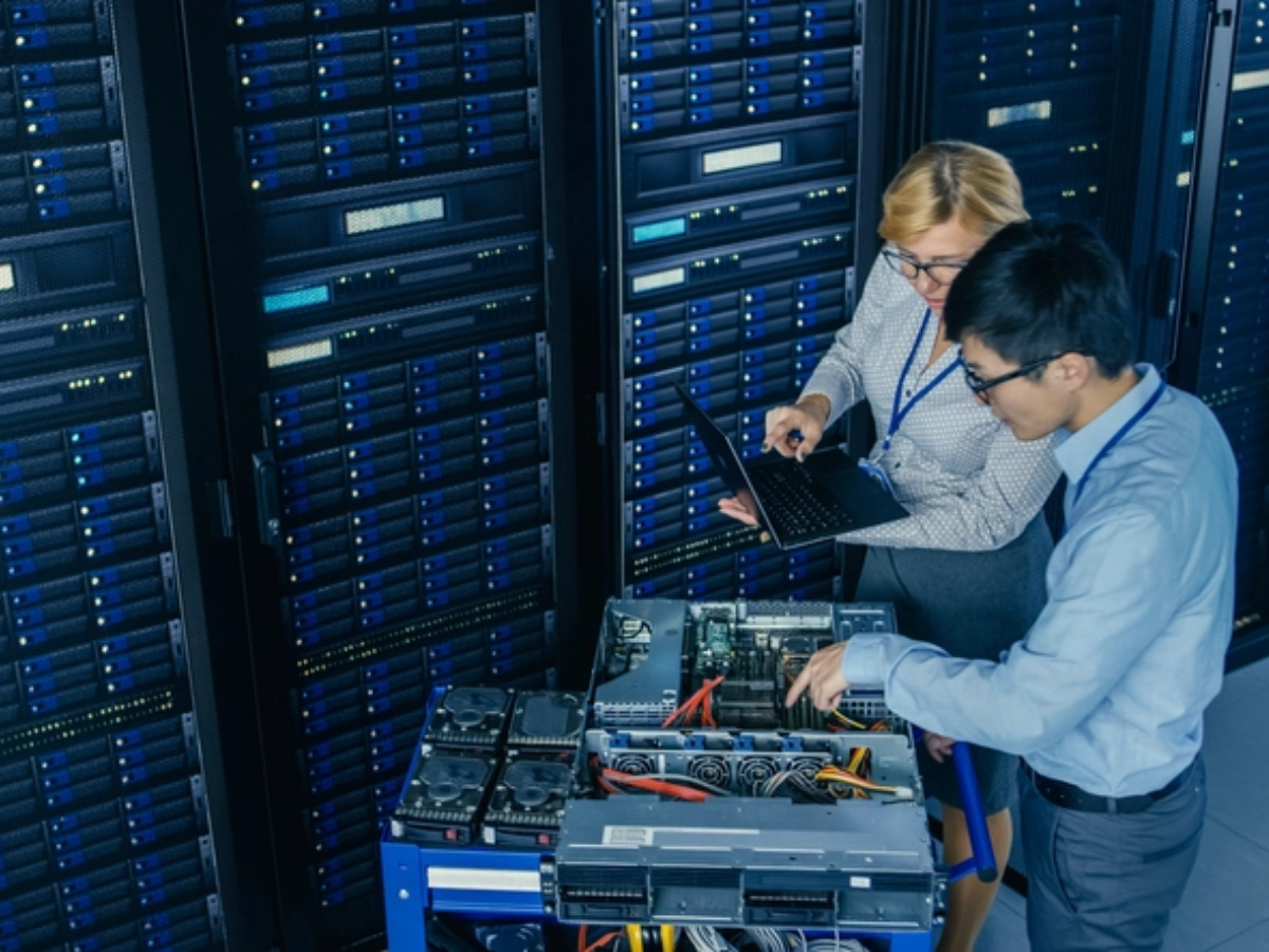Two data center technicians configuring 100G QSFP28 breakout connections to 25G SFP28 transceivers in server racks with blue LED indicators