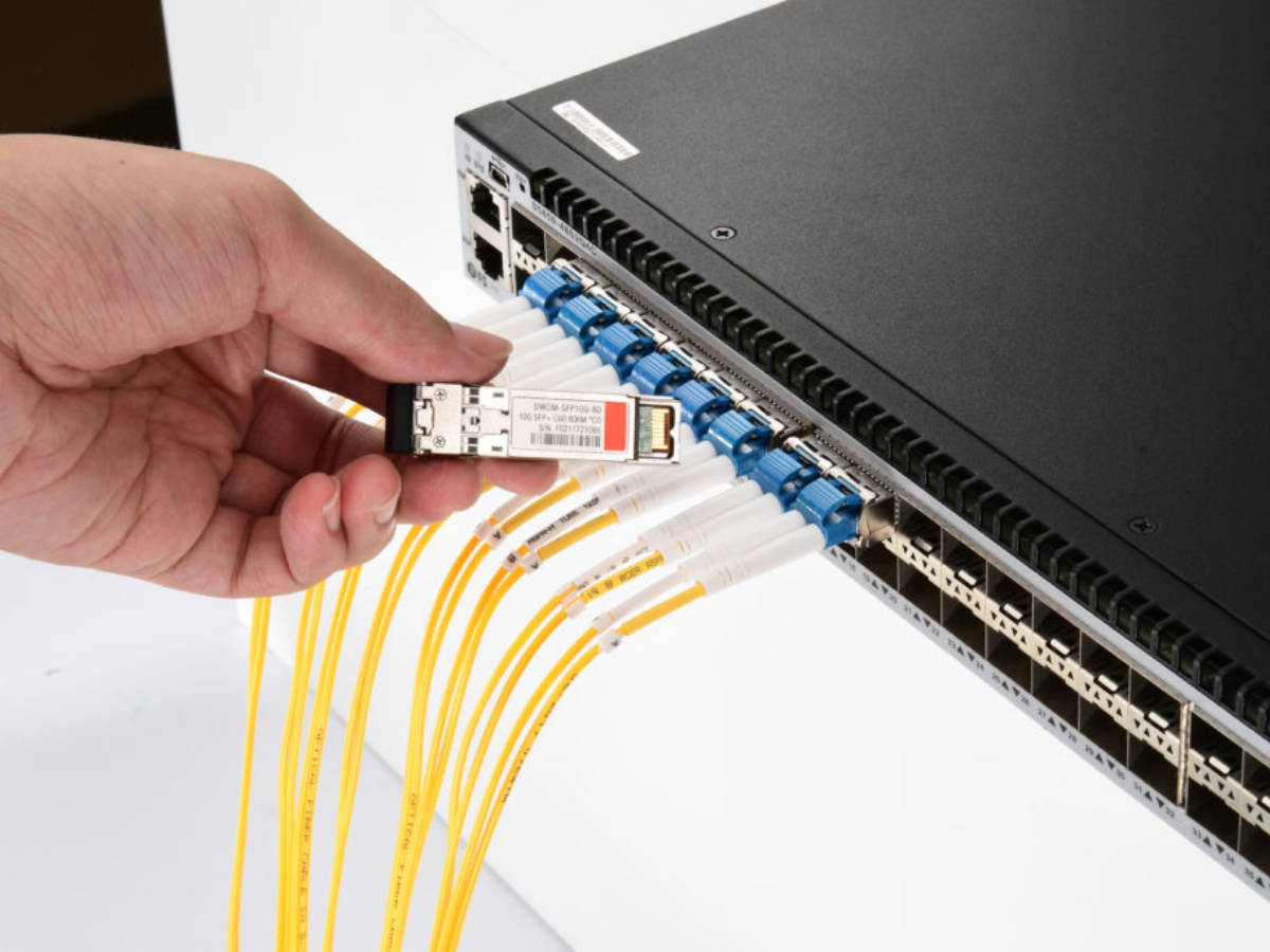 Network technician installing SFP fiber optic transceiver into switch with blue LC connectors and yellow fiber cables for squelch configuration