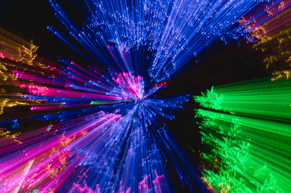 Colorful fiber optic light transmission showing blue, pink, green, and yellow laser beams radiating through optical fibers demonstrating VCSEL, FP, and DFB laser technologies